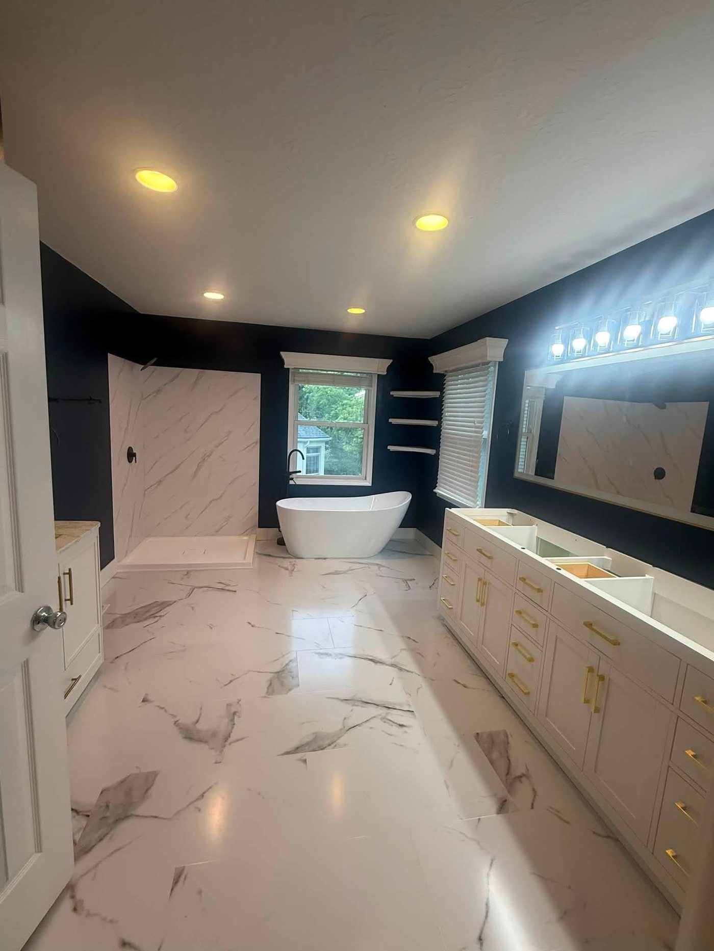 Completed primary bathroom with deep navy painted walls, freestanding tub, and marble-look shower